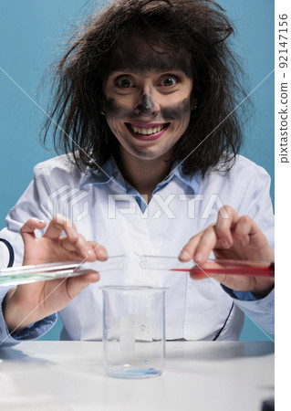 Crazy foolish biochemist with beakers experimenting new formula discovered by mistake in laboratory explosion. Insane maniac chemist mixing toxic unidentified compounds using glass tubes and beaker Crazy foolish biochemist with beakers experimenting new formula discovered by mistake in laboratory explosion. Insane maniac chemist mixing toxic unidentified compounds using glass tubes and beaker 92147156