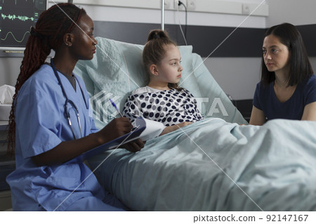 African american nurse consulting hospitalized little girl resting in pediatric healthcare clinic ward. Ill kid recovering from disease while medical staff doing health condition checkup. African american nurse consulting hospitalized little girl resting in pediatric healthcare clinic ward. Ill kid recovering from disease while medical staff doing health condition checkup. 92147167