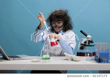 Mad scientist with wild appearance acting silly after lab explosion. Portrait of crazy amusing chemist acting funny and having dirty face and messy hair while sitting at desk and looking at camera Mad scientist with wild appearance acting silly after lab explosion. Portrait of crazy amusing chemist acting funny and having dirty face and messy hair while sitting at desk and looking at camera 92147173