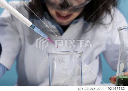 Close up of crazy lab worker dripping blood drops in glass beaker while conducting dangerous test. Lunatic silly looking maniac biochemist using dropper to experiment with toxic chemical compounds. 92147182