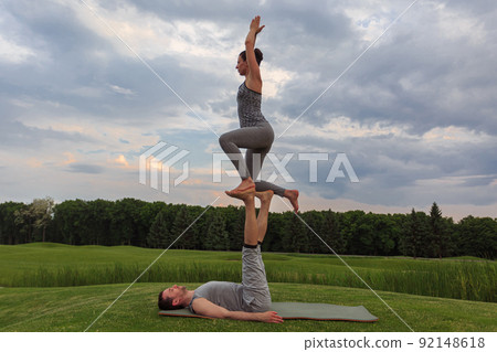 Young couple doing acro yoga in park. Man lying on grass and balancing woman in his feet Young couple doing acro yoga in park. Man lying on grass and balancing woman in his feet 92148618