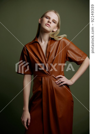 Trendy stylish offer for your brand. Fashion gorgeous young blonde lady holding hand on waist dress in leather trench coat serious looks at camera posing isolated on over olive green studio background 92149389