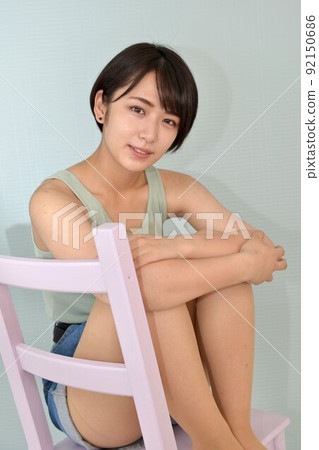 A smiling young woman in a camisole sitting in a chair and relaxing 92150686