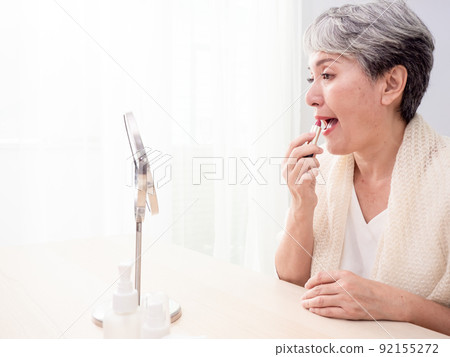 Portrait of mature aged asian woman 60s applying lipstick looking at mirror. Portrait of mature aged asian woman 60s applying lipstick looking at mirror. 92155272