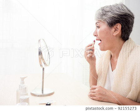 Portrait of mature aged asian woman 60s applying lipstick looking at mirror. Portrait of mature aged asian woman 60s applying lipstick looking at mirror. 92155273