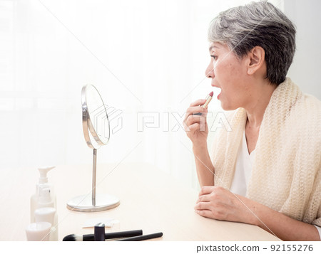 Portrait of mature aged asian woman 60s applying lipstick looking at mirror. Portrait of mature aged asian woman 60s applying lipstick looking at mirror. 92155276