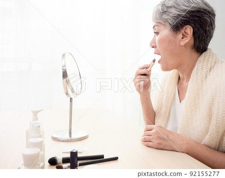 Portrait of mature aged asian woman 60s applying lipstick looking at mirror. Portrait of mature aged asian woman 60s applying lipstick looking at mirror. 92155277