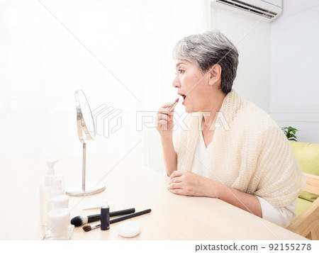 Portrait of mature aged asian woman 60s applying lipstick looking at mirror. Portrait of mature aged asian woman 60s applying lipstick looking at mirror. 92155278