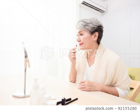 Portrait of mature aged asian woman 60s applying lipstick looking at mirror. Portrait of mature aged asian woman 60s applying lipstick looking at mirror. 92155280
