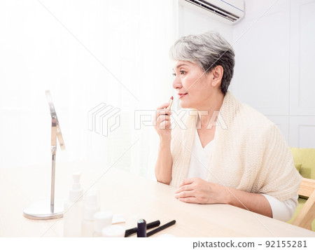 Portrait of mature aged asian woman 60s applying lipstick looking at mirror. Portrait of mature aged asian woman 60s applying lipstick looking at mirror. 92155281