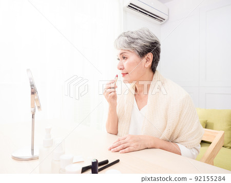 Portrait of mature aged asian woman 60s applying lipstick looking at mirror. Portrait of mature aged asian woman 60s applying lipstick looking at mirror. 92155284
