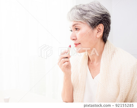 Portrait of mature aged asian woman 60s applying lipstick looking at mirror. Portrait of mature aged asian woman 60s applying lipstick looking at mirror. 92155285