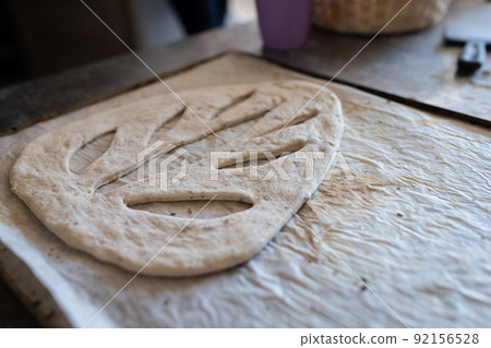 A baker shapes and cuts traditional French Fougasse bread. Front view. 92156528