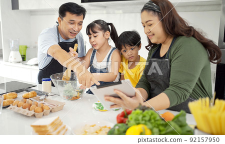 Happy asian parents and their kids having fun while cooking and following recipe on the internet. 92157950