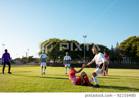 Multiracial player holding hand and assisting injured opponent to get up during match at playground Multiracial player holding hand and assisting injured opponent to get up during match at playground 92158480