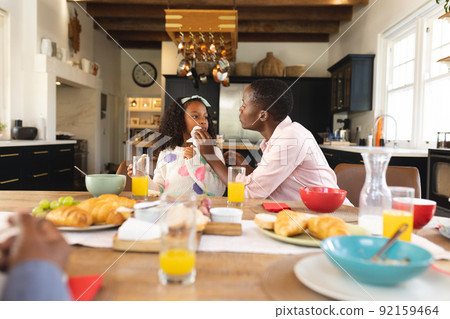 Image of happy african american girl eating breakfast with mother Image of happy african american girl eating breakfast with mother 92159464