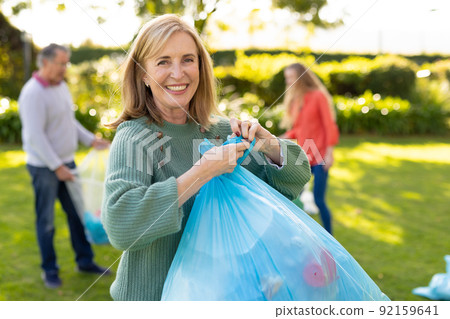 Image of happy caucasian woman with rubbish bags in garden 92159641