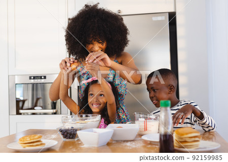 Multiracial mother with afro hair breaking egg with daughter in bowl while making breakfast on table Multiracial mother with afro hair breaking egg with daughter in bowl while making breakfast on table 92159985