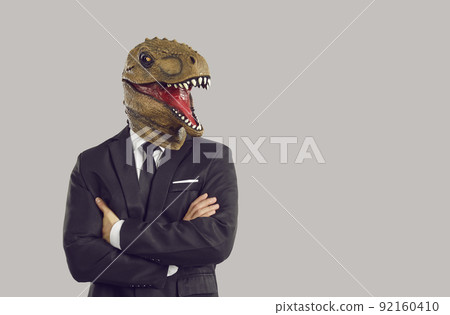 Funny man with dinosaur mask on head stands in studio with arms crossed dressed in business suit 92160410