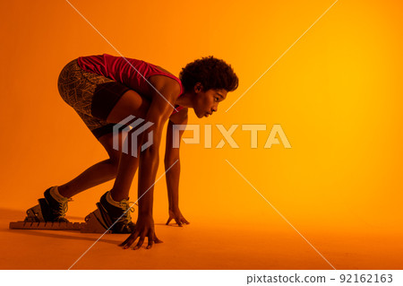 Image of african american female athlete preparing for run in neon orange lighting 92162163