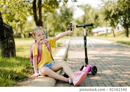 Portrait of a little beautiful schoolgirl girl using a mobile phone and taking a selfie 92162340