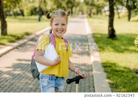A beautiful little girl rides a scooter on her way back to school A beautiful little girl rides a scooter on her way back to school 92162345
