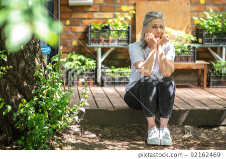 A woman in white tshirt sitting outside and looking thoughtful A woman in white tshirt sitting outside and looking thoughtful 92162469