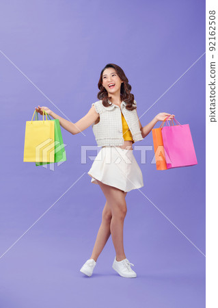Happy young woman with color shopping bags, over purple background Happy young woman with color shopping bags, over purple background 92162508