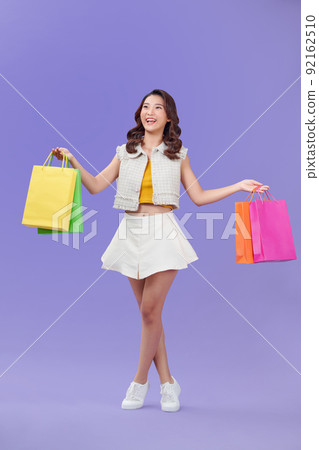 Woman holding shopping bags against a purple background Woman holding shopping bags against a purple background 92162510