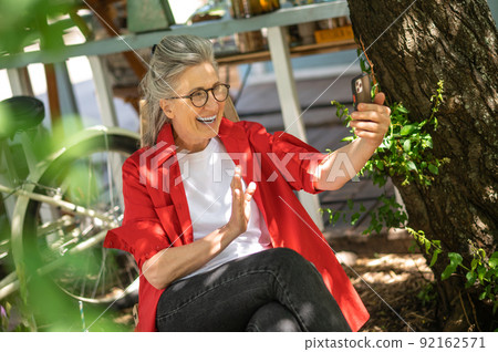 A woman in red shirt sitting outside and spending time online A woman in red shirt sitting outside and spending time online 92162571