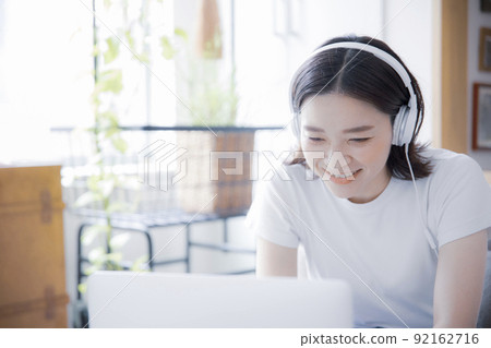 Japanese women doing online lessons and remote work with earphones and laptops in a bright room 92162716