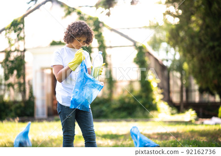 Curly-haired teen gathering garbage in the park Curly-haired teen gathering garbage in the park 92162736