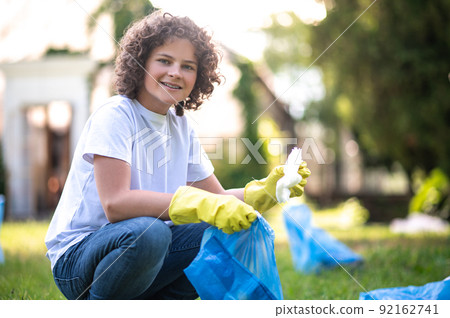 Curly-haired teen gathering garbage in the park Curly-haired teen gathering garbage in the park 92162741