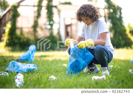 Curly-haired teen gathering garbage in the park 92162743