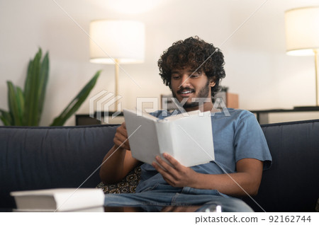 Curly-haired indian guy reading a book and looking involved 92162744