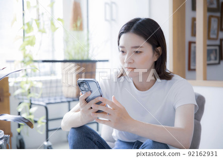 Japanese woman browsing the internet on her smartphone in a bright room 92162931