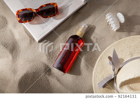 magazine, sunglasses and sunscreen on beach sand 92164131