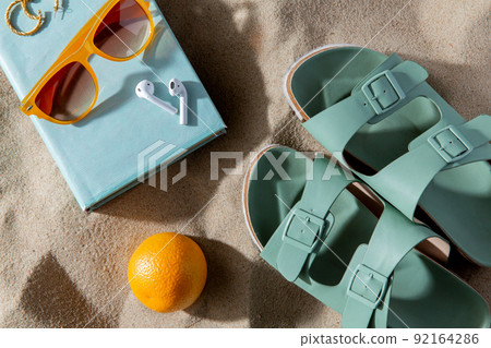 slippers, orange, earbuds and sunglasses on beach 92164286