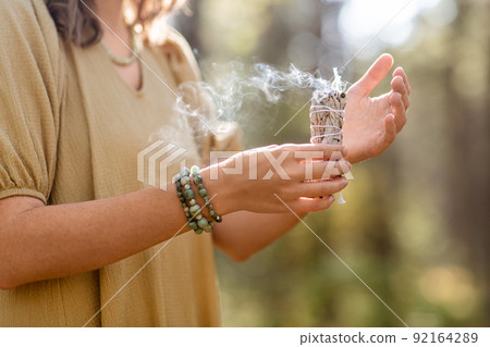 woman with sage performing magic ritual in forest 92164289