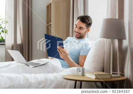 man with laptop working in bed at home bedroom 92164387