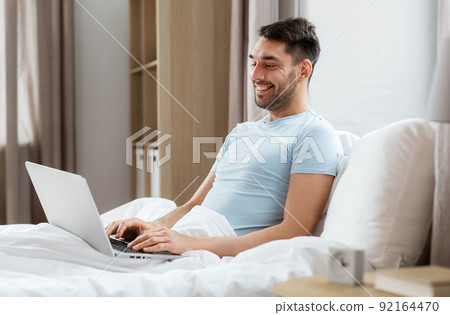 man with laptop in bed at home bedroom man with laptop in bed at home bedroom 92164470