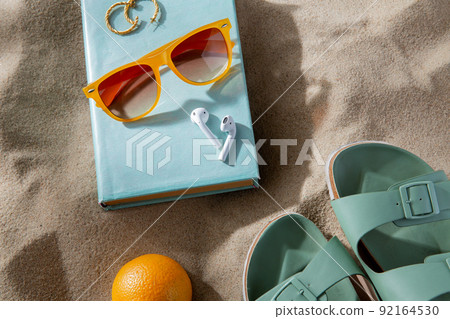 slippers, orange, earbuds and sunglasses on beach slippers, orange, earbuds and sunglasses on beach 92164530