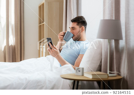 happy man with smartphone in bed at home happy man with smartphone in bed at home 92164531