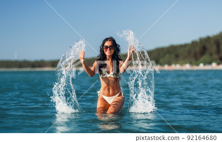 woman in bikini splashing sea water on beach 92164680