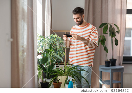 man with smartphone and flowers at home man with smartphone and flowers at home 92164832