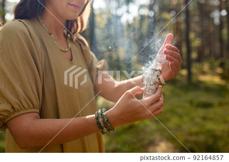 woman with sage performing magic ritual in forest 92164857