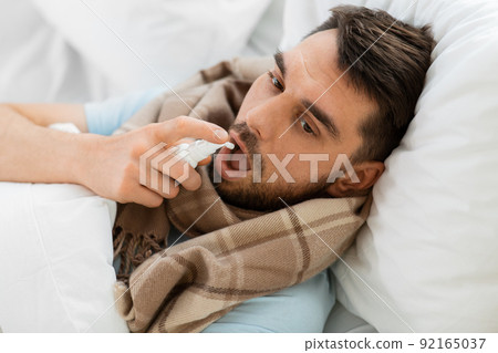 sick man with oral spray lying in bed at home sick man with oral spray lying in bed at home 92165037