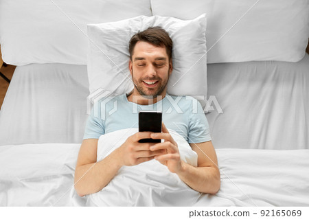 man with smartphone in bed in morning at home man with smartphone in bed in morning at home 92165069
