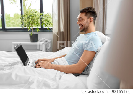 man with laptop in bed at home bedroom 92165154