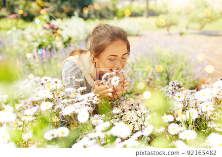 happy woman smelling chamomile flowers in garden 92165482